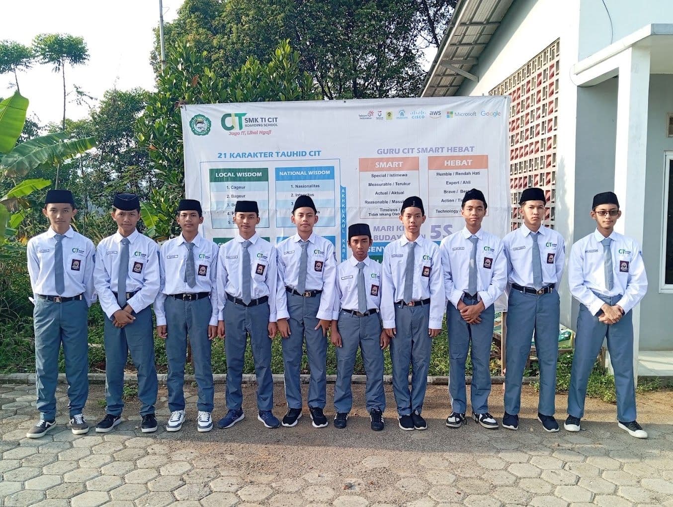 Santri CIT Manahilul Ilmi berseragam berdiri di depan banner sekolah